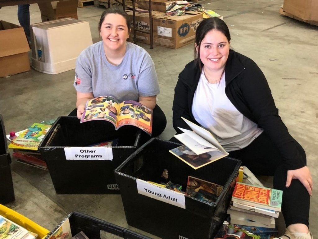 Two VISTA members sorting through boxes of children's books.