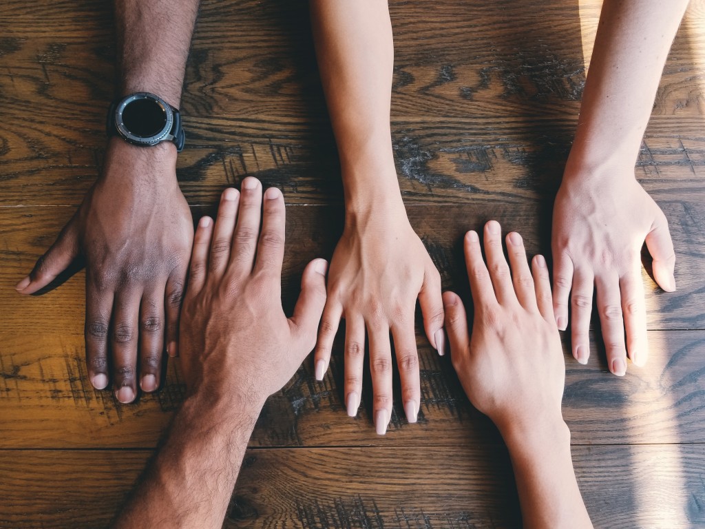 Human hands of varying skin tone resting on a wooden table